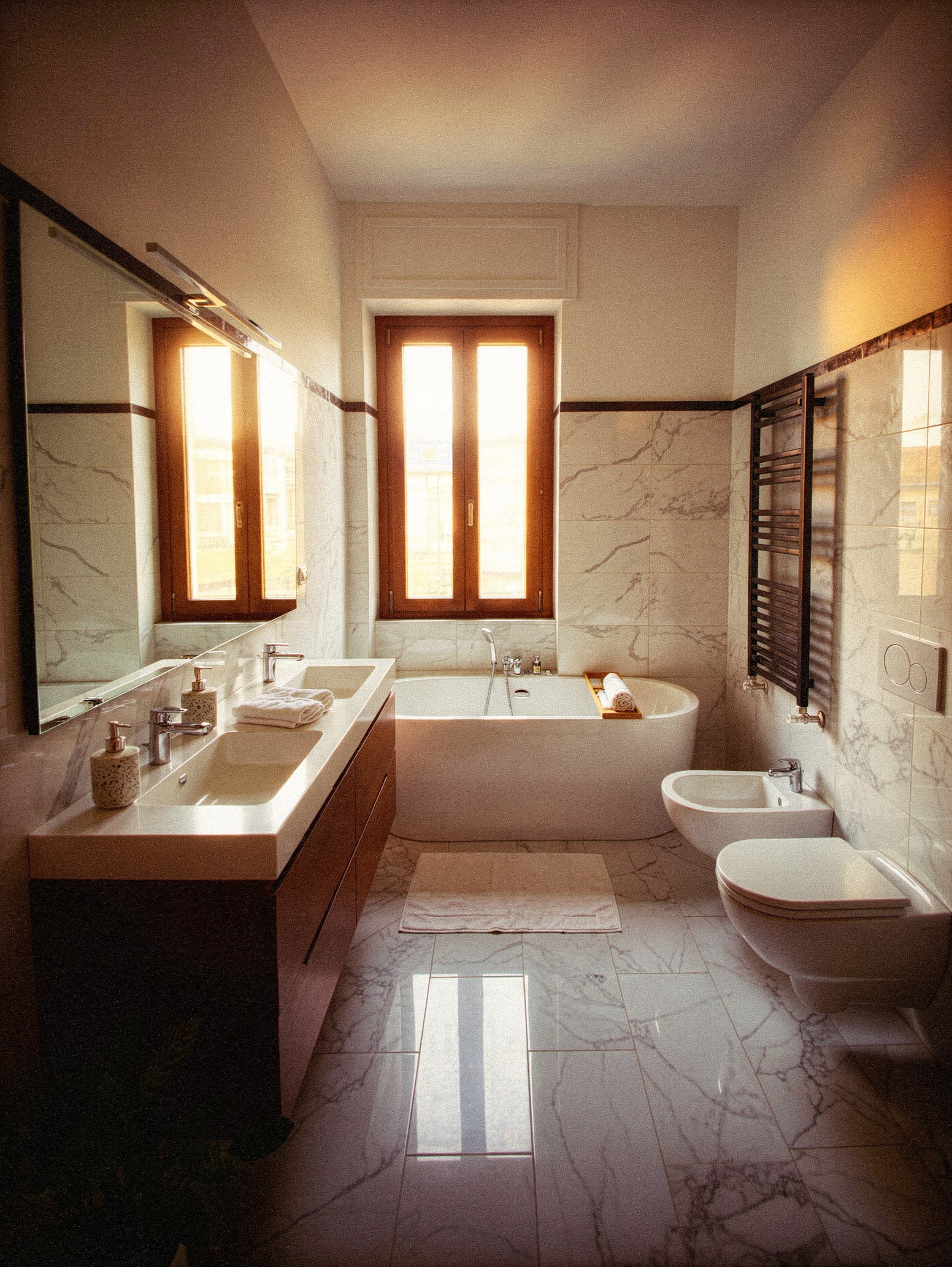 Bagno in marmo Calacatta; doppio lavabo su mobile sospeso in legno; vasca freestanding ovale; scaldasalviette nero opaco; serramento in legno
